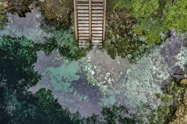 Aerial view of Madison Blue Spring State Park with stairs going down into the clear blue water with rocks and vegetation around in the town of Lee, Florida, United States. - AAEF21735