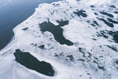 Abstract aerial view of amazingly shaped snow remains with gaps, on the ice of a frozen lake in winter, Reykjanes, Iceland. - AAEF21772