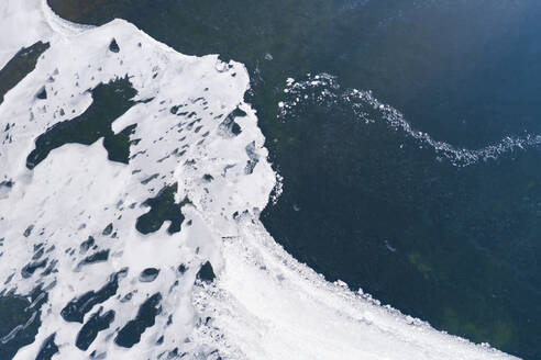 Abstract aerial view of amazingly shaped snow remains with gaps, on the ice of a frozen lake in winter, Reykjanes, Iceland. - AAEF21773