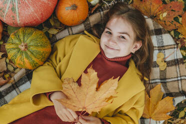 Smiling girl holding leaf and lying on blanket in garden - YTF01047
