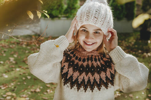 Lächelndes Mädchen mit Strickmütze im Garten stehend - YTF01059
