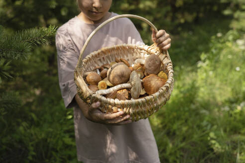 Girl holding basket of mushrooms in forest - LESF00418