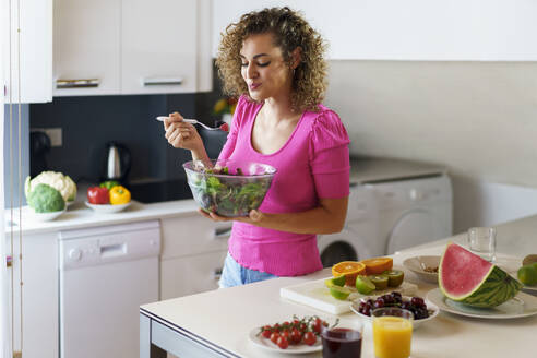 Lächelnde Frau isst Salat in der Küche zu Hause - JSMF02877