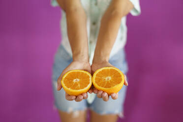 Hands of woman holding slices of oranges against magenta background - JSMF02881