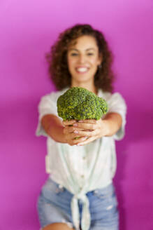 Happy woman holding broccoli and standing against magenta background - JSMF02888