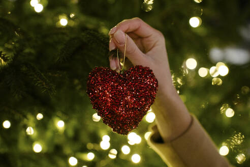 Hand einer Frau hält herzförmige Weihnachtsdekoration - YBF00099