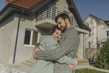 Lächelndes Paar, das sich vor seinem neuen Haus umarmt - OSF01957