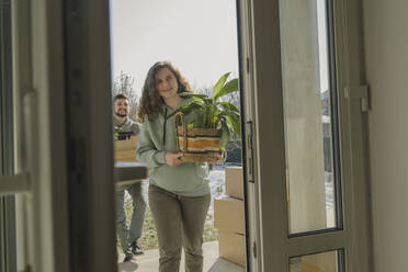 Glückliche Frau trägt Zimmerpflanze in ihr neues Zuhause - OSF01960