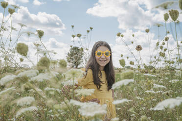 Lächelndes Mädchen mit Sonnenbrille inmitten von Blumen auf einem Feld - OSF01963