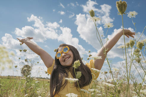 Glückliches Mädchen mit erhobenen Händen, das sich an einem Blumenfeld erfreut - OSF01968