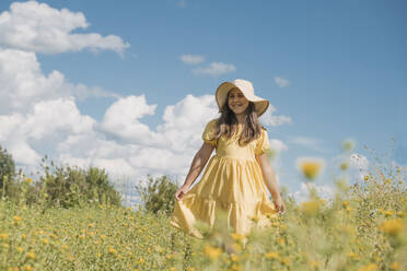 Lächelndes Mädchen mit Hut und in einem Blumenfeld stehend - OSF01972