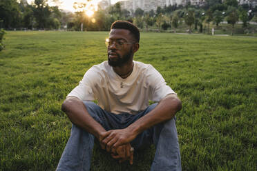 Nachdenklicher Mann sitzt im Gras in einem Park - YBF00106