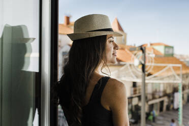 Nachdenkliche junge Frau mit Hut schaut durch das Fenster - DCRF01646