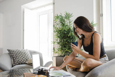 Smiling woman with coffee cup using laptop in apartment - DCRF01661