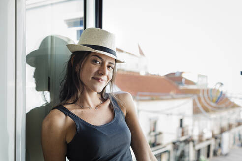 Lächelnde Frau mit Hut, die sich an ein Fenster lehnt - DCRF01707