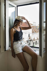 Lächelnde Frau, die ihren Hut berührt und auf dem Fensterbrett sitzt - DCRF01709