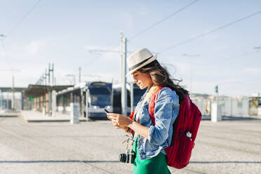 Smiling young woman wearing hat using smart phone on sunny day - DCRF01727