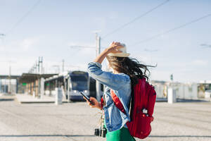 Frau mit Hut steht mit Smartphone an einem sonnigen Tag - DCRF01728
