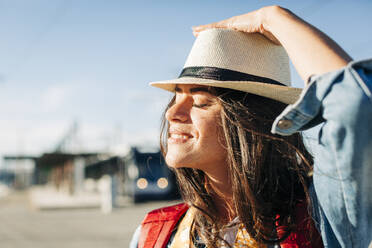 Smiling young woman wearing hat with eyes closed on sunny day - DCRF01731