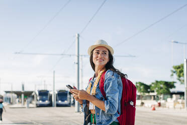 Glückliche junge Frau mit Mobiltelefon an einem sonnigen Tag - DCRF01732