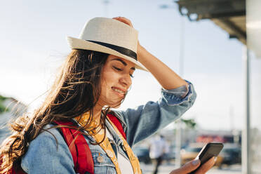 Glückliche junge Frau mit Hut, die ein Mobiltelefon benutzt - DCRF01735
