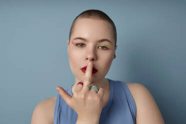 Rude woman with middle finger on lips against blue background - KPEF00171