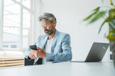 Businessman using smart phone sitting at office - JOSEF20495