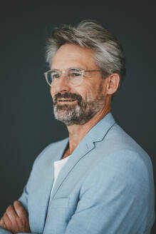 Contemplative businessman wearing eyeglasses against teal background - JOSEF20502