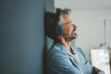 Smiling businessman listening to music at office - JOSEF20514