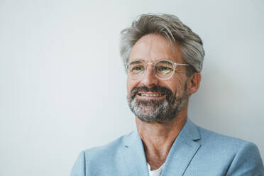 Smiling businessman wearing eyeglasses in front of white wall - JOSEF20517