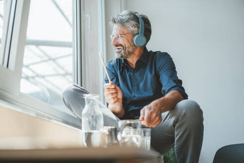 Glücklicher Geschäftsmann spielt mit Stöcken und hört Musik im Büro - JOSEF20534