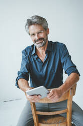 Businessman with tablet PC sitting on chair at office - JOSEF20536