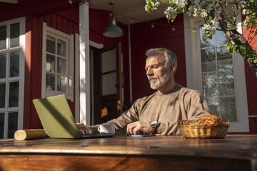 Mature freelancer working on laptop sitting outside house - VPIF08352