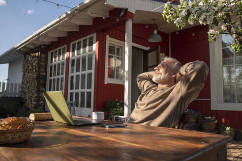 Freelancer with laptop on table resting outside house - VPIF08355