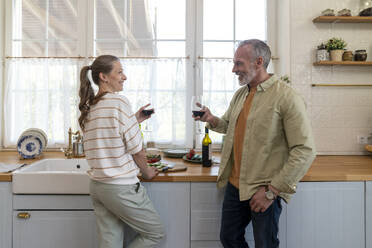 Happy couple enjoying wine standing in kitchen at home - VPIF08365