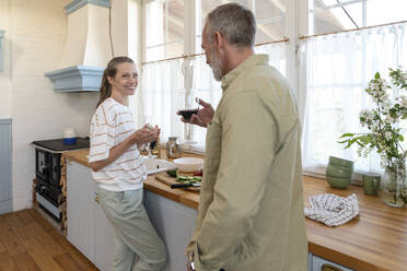 Smiling woman having wine with man standing in kitchen at home - VPIF08366