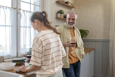 Happy man having wine by woman preparing food in kitchen at home - VPIF08367
