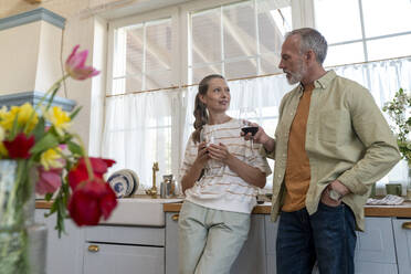 Couple having wine and talking to each other standing in kitchen at home - VPIF08368