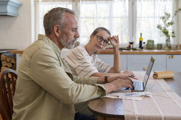 Woman discussing with man preparing bills over laptop at home - VPIF08388