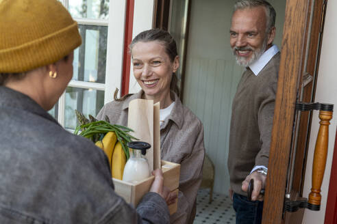 Delivery person giving groceries to couple standing at door - VPIF08403