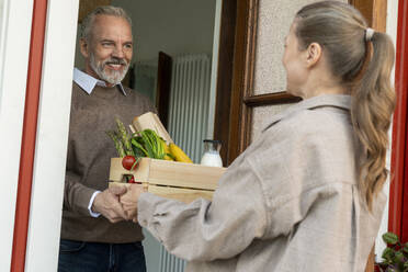 Lächelnder Mann, der eine Kiste mit Lebensmitteln von einer Frau an der Tür entgegennimmt - VPIF08406