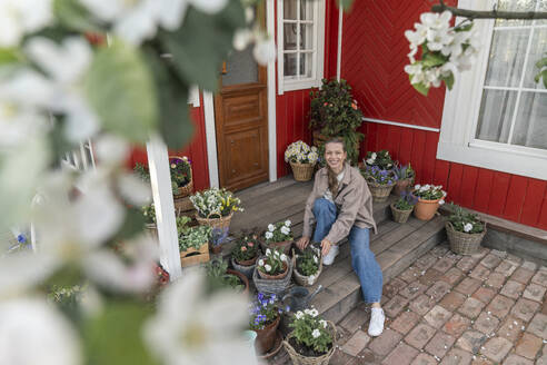 Lächelnde Frau sitzt auf Veranda inmitten von Pflanzen - VPIF08456