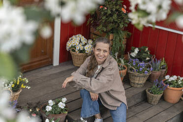 Smiling mature woman sitting by flowering plants on porch - VPIF08457