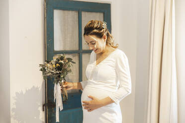 Schwangere Braut, die zu Hause ihren Unterleib berührt - PCLF00649