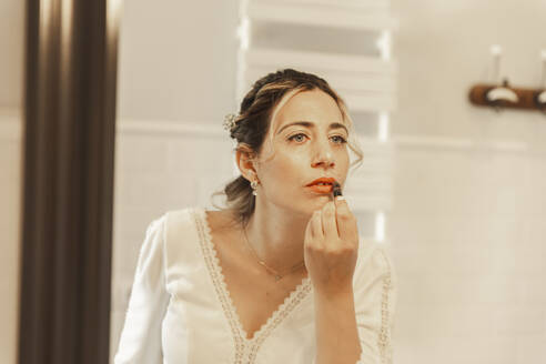 Bride applying lipstick looking in mirror at home - PCLF00650