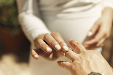Hand of bride putting wedding ring on groom's finger - PCLF00655
