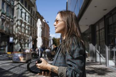 Lächelnde Frau mit Sonnenbrille in der Nähe eines Gebäudes in der Stadt - NDEF00967