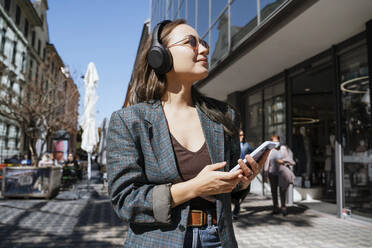 Thoughtful woman holding smart phone near building - NDEF00969