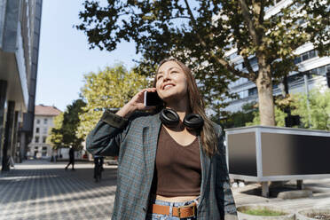 Lächelnde Frau, die an einem sonnigen Tag mit ihrem Smartphone telefoniert - NDEF00981