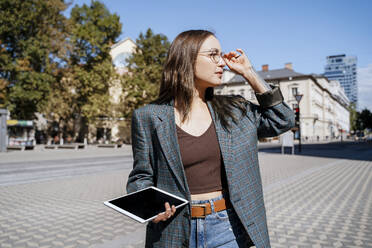 Thoughtful woman standing with tablet PC in city on sunny day - NDEF00990